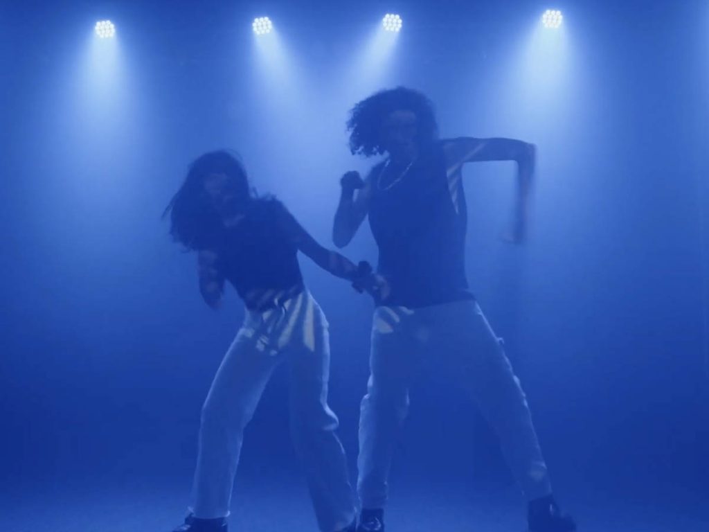 In gedämpftem blauen Licht sind zwei Tänzer*innen in einer totalen zu sehen. Es handelt sich um die Deaf Performer*innen JoNu, die eine Choreografie aufführen.
