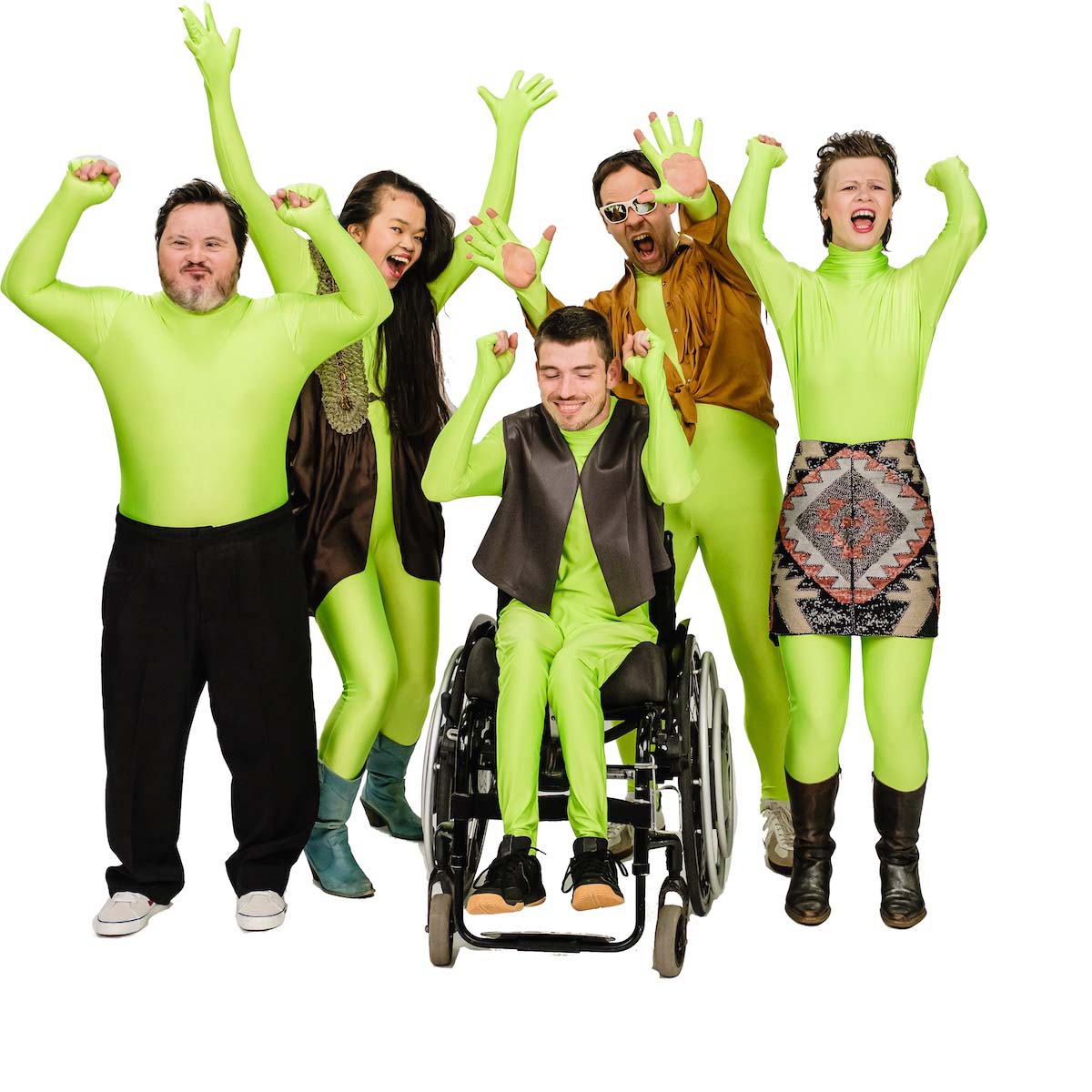 The band 21 downbeat can be seen, consisting of two women and three men in tight light green full-body suits, over each of which they wear another, everyday item of clothing such as trousers, waistcoat, skirt, shirt and blouse, jubilantly throwing their hands up and showing facial expressions of joy - with open mouths and smiles. Four of the people are standing next to and behind a man sitting in a wheelchair in the centre of the picture. The background is completely white, the picture looks cropped.